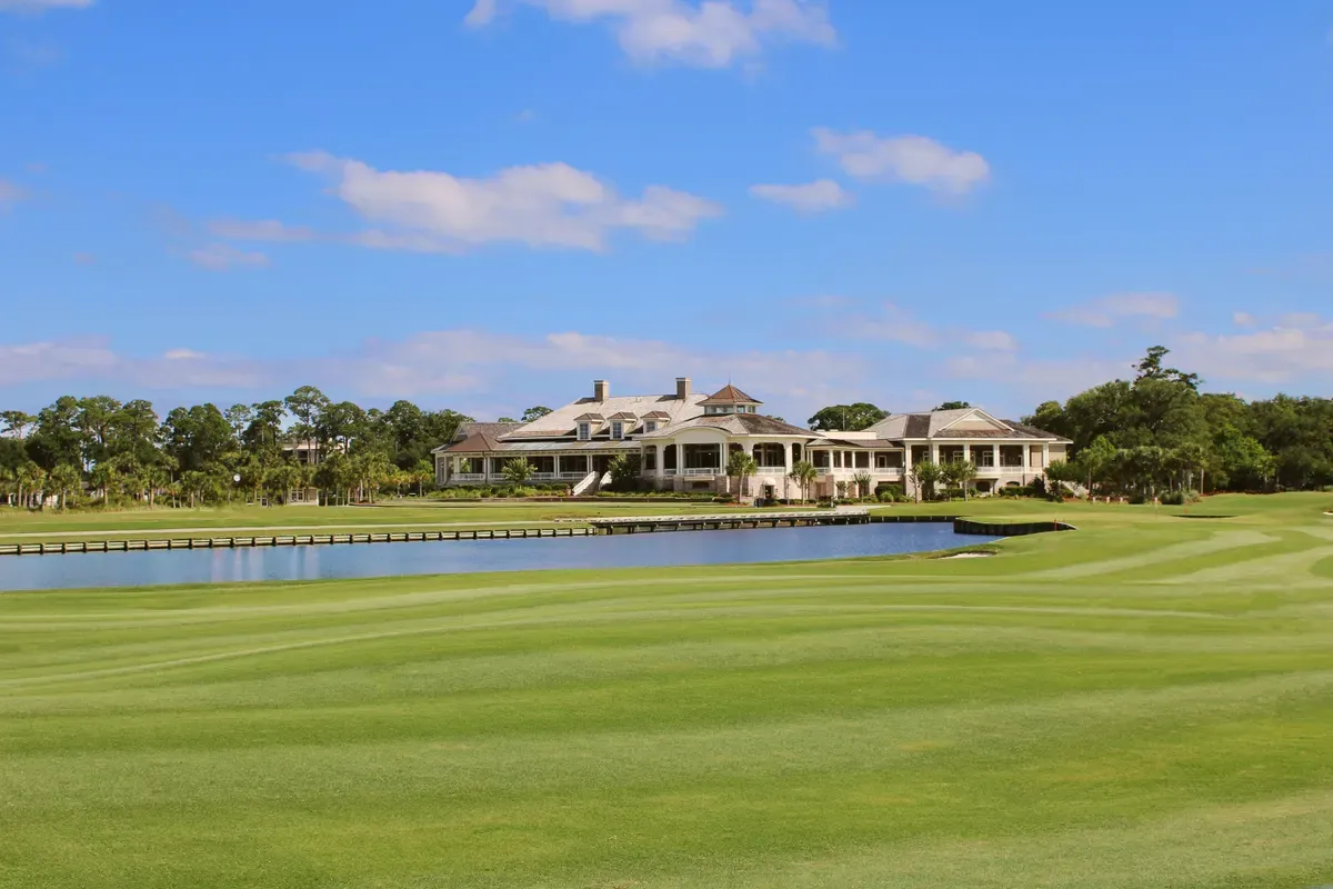 Golf course fairway and pond with a large clubhouse in the distance on a sunny day