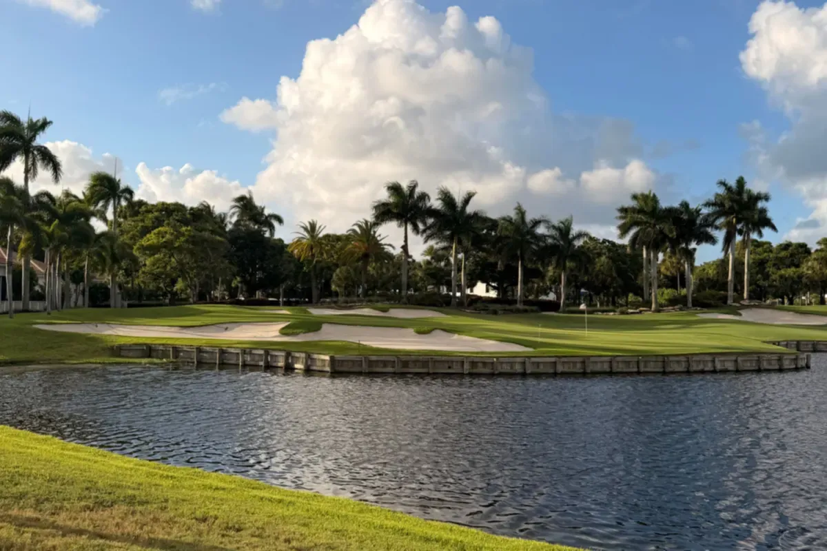 Golf fairway beside a lake with palm trees and sand bunkers under a partly cloudy sky in Florida